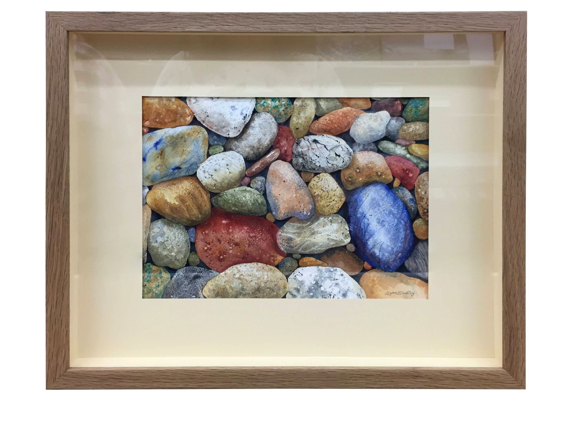 Framed watercolor of colorful pebbles, arranged closely together, brown frame, tan matting.