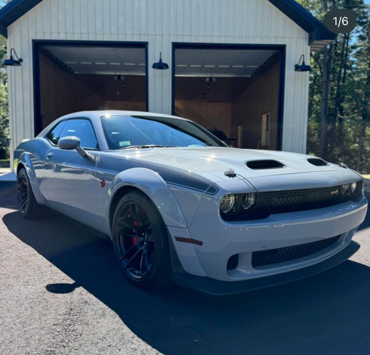 A white dodge challenger is parked in front of a garage.