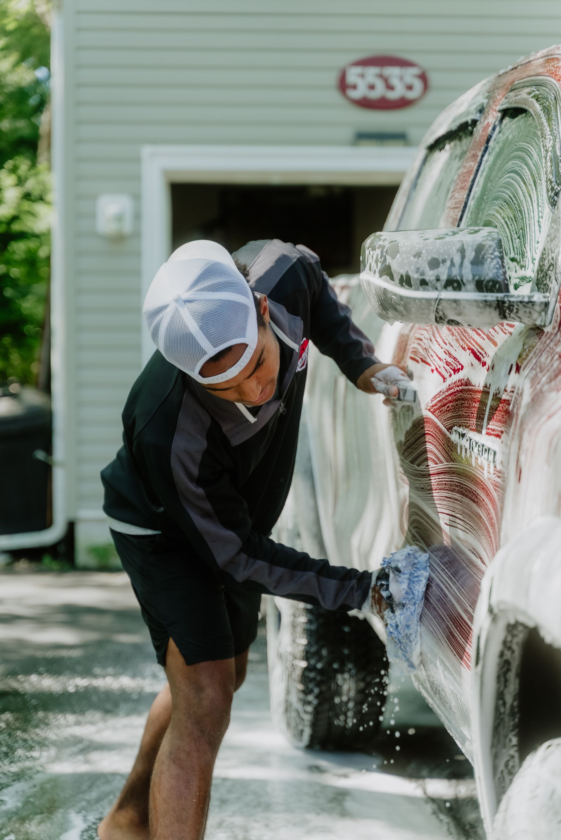 A man is washing a car with a red sponge.