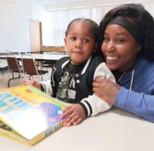 Woman and child reading a book together at a table. Both are smiling.