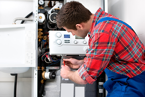 a man in a plaid shirt and blue overalls is working on a boiler .
