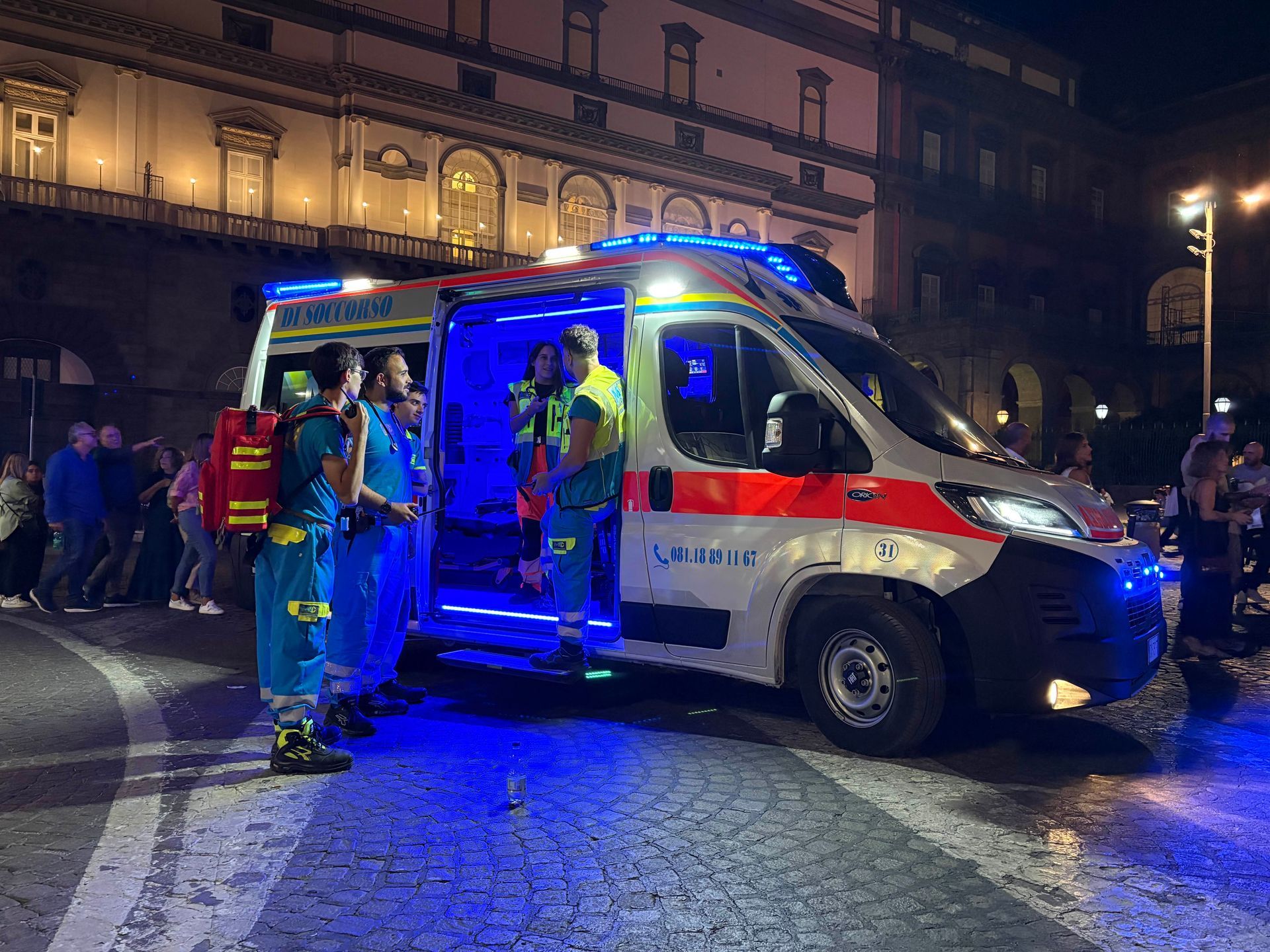 Ambulanza con paramedici di notte, illuminata da luci blu, davanti a un edificio.
