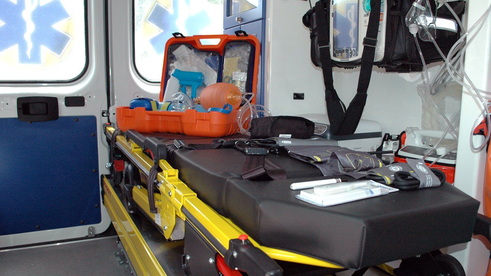Interno di un'ambulanza con una barella, attrezzature mediche e una cassa arancione aperta.
