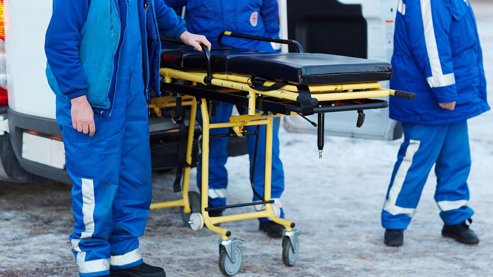 Tre operatori sanitari a bordo di un'ambulanza con una barella gialla e nera.