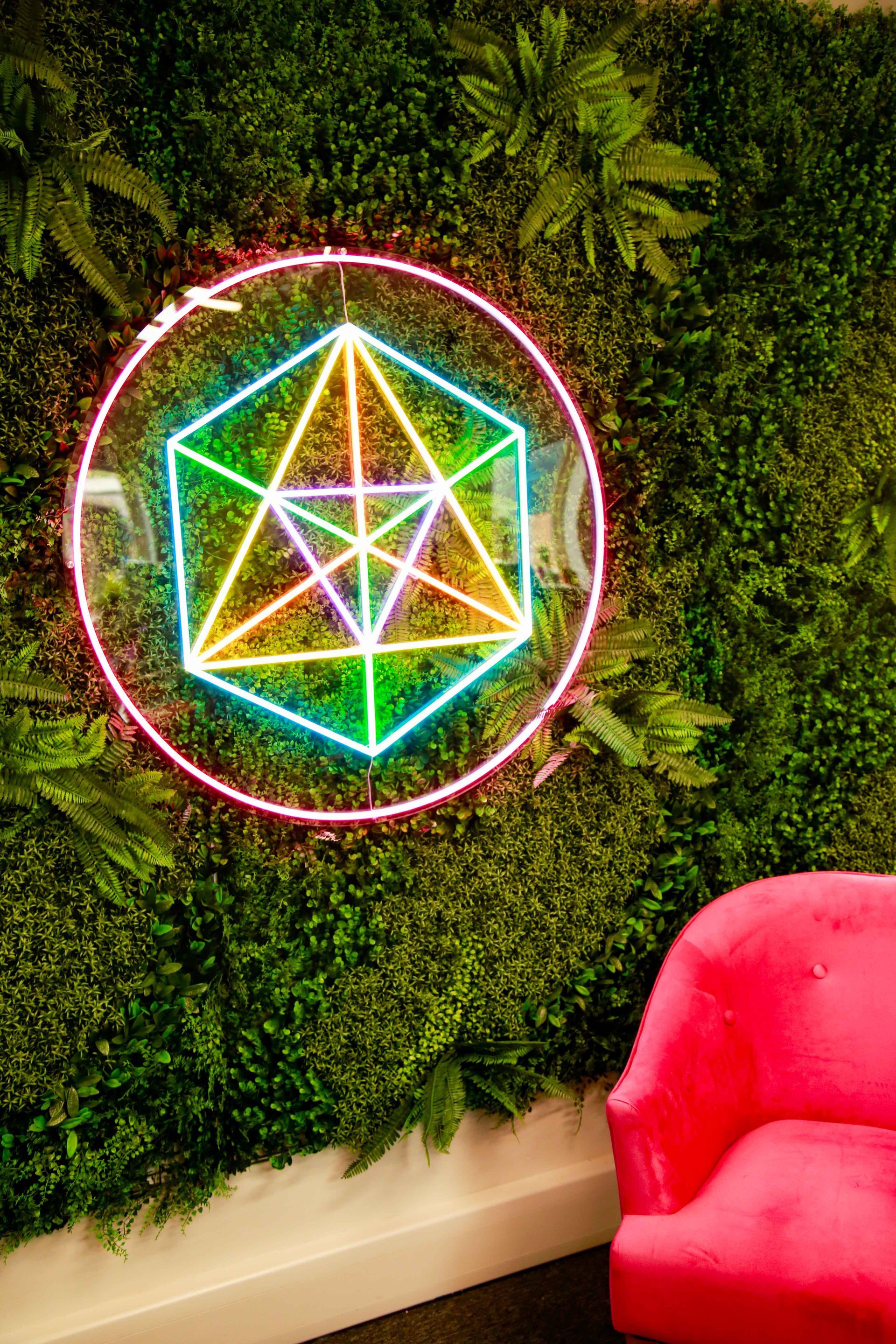 Neon sign of a geometric shape on a green wall with a pink chair.