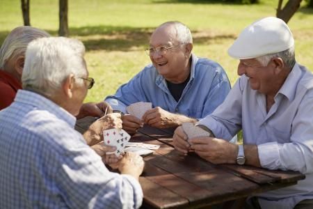Three seniors playing cards at a picnic table in a sunny park