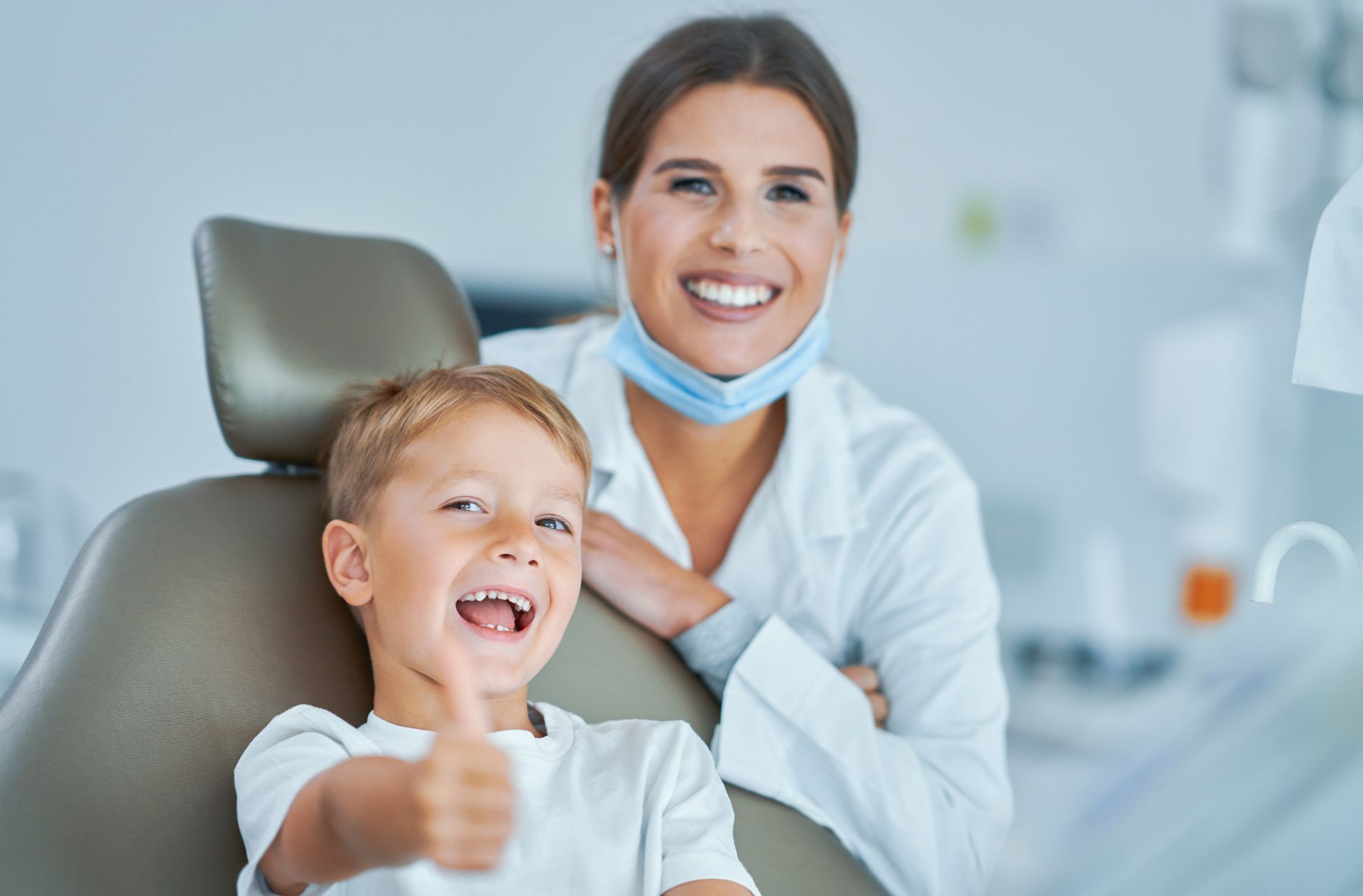 A little boy is sitting in a dental chair and giving a thumbs up.