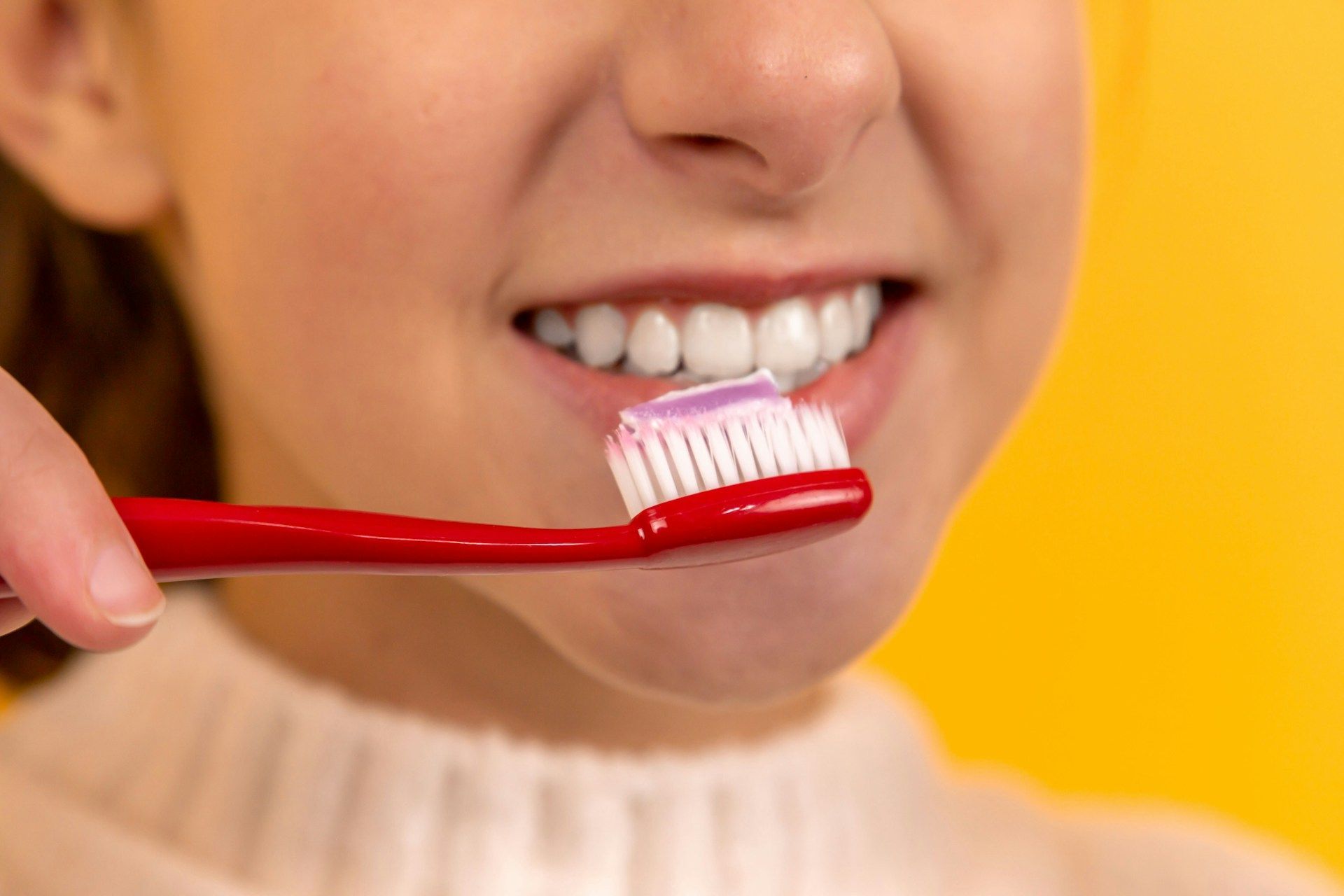 A young woman is brushing her teeth with a red toothbrush.