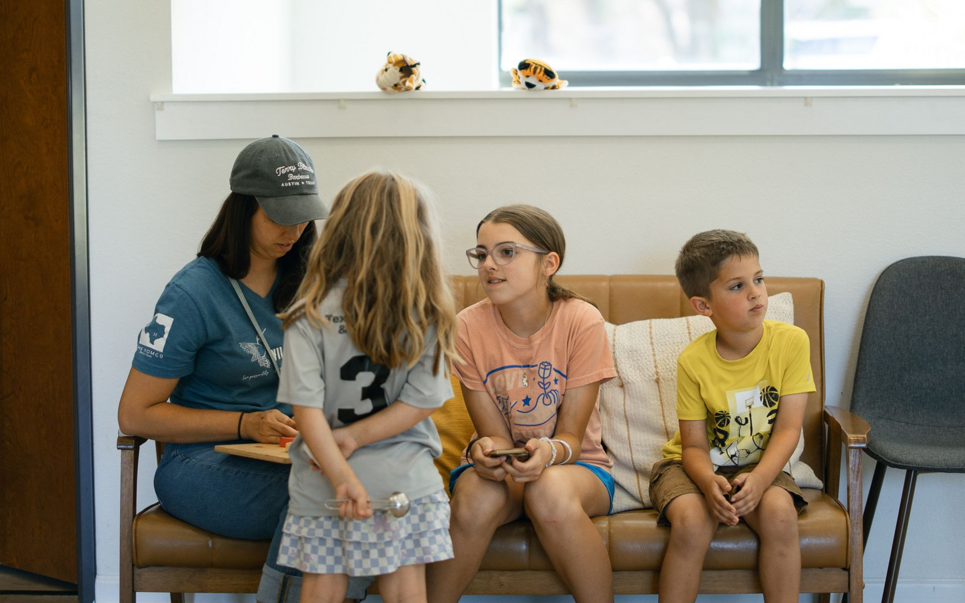 Woman sitting with her three children on a bench indoors, waiting.