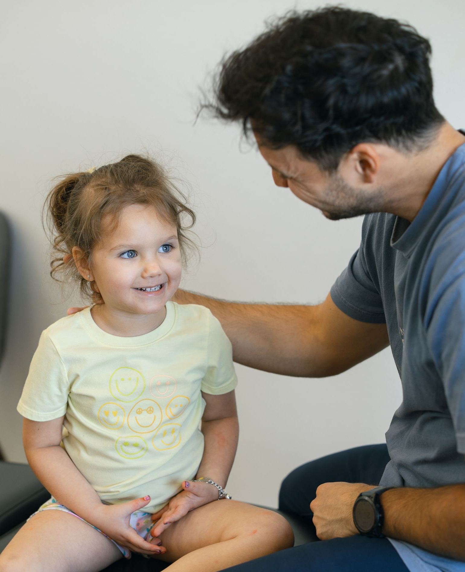 Young child smiles at Dr. Rudy, who has his hand on her shoulder, in Living Water Chiropractic.