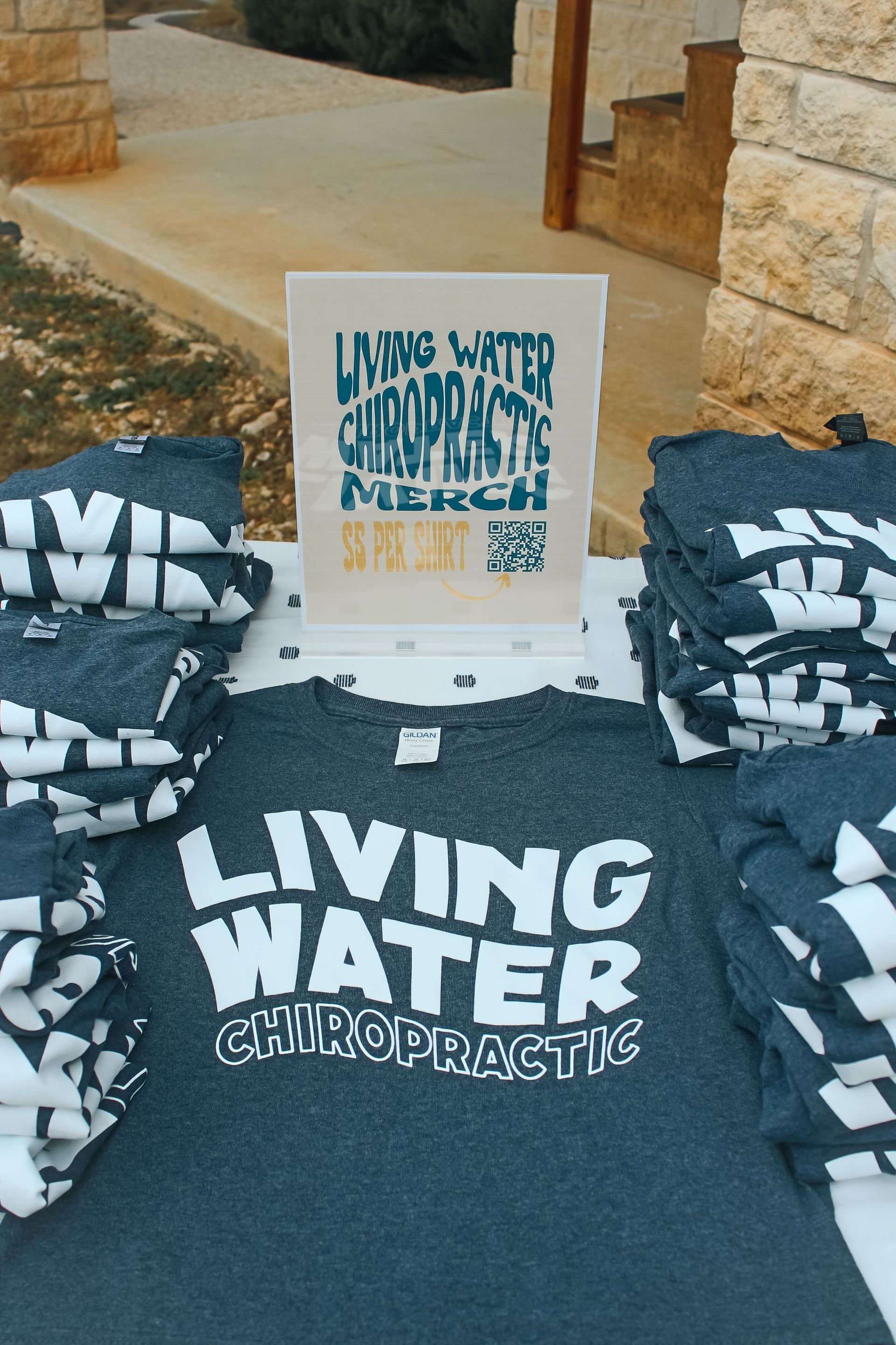 A table displays stacks of charcoal gray t-shirts featuring the white text 