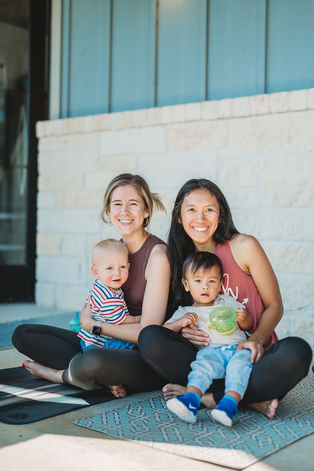 Two women sitting on a porch with two small children, smiling at the camera.