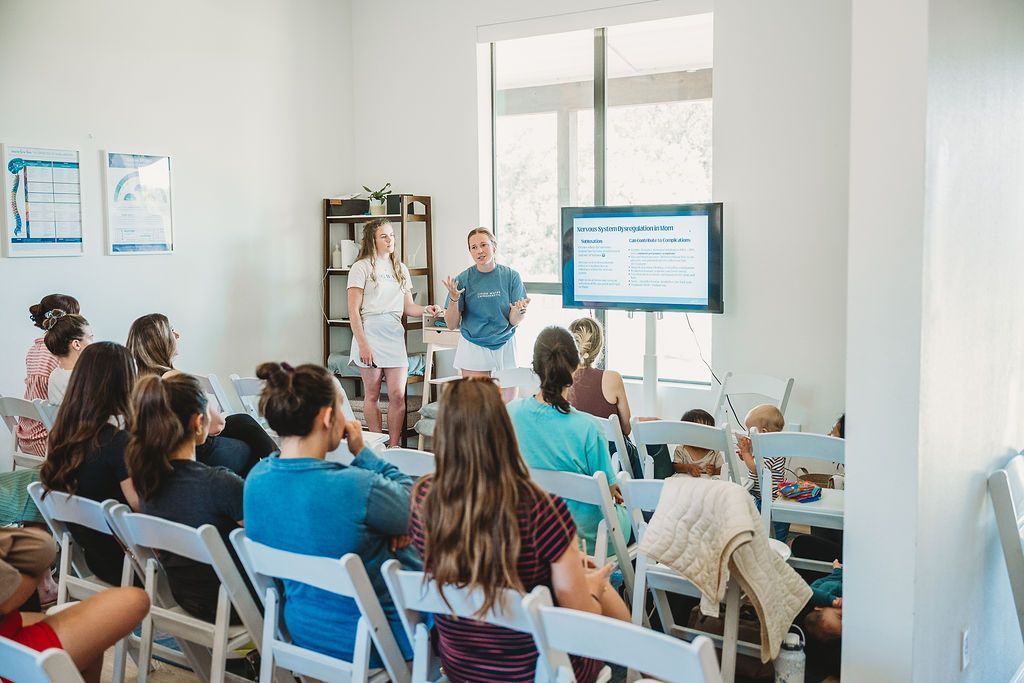 People seated in a bright meeting room watching a presentation on a large screen.