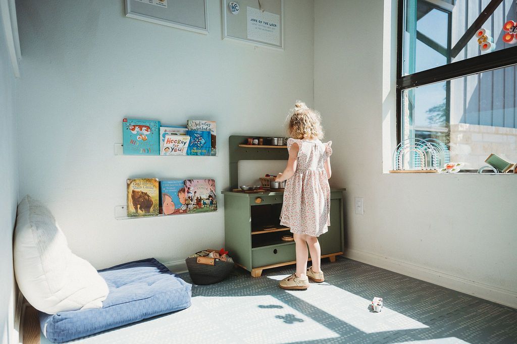 Child standing by a shelf in a bright playroom with a beanbag chair and sunlight through the window