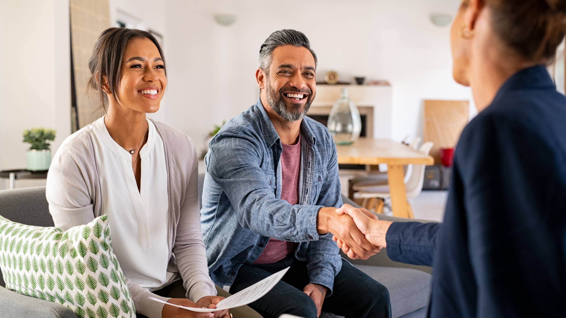 A man and woman are shaking hands with a real estate agent while sitting on a couch.