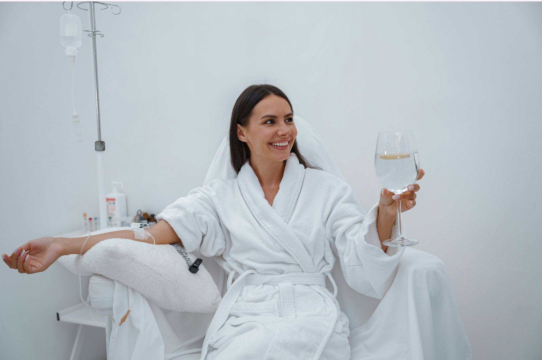 Woman in a white robe reclining in a spa chair, smiling and holding a glass of water