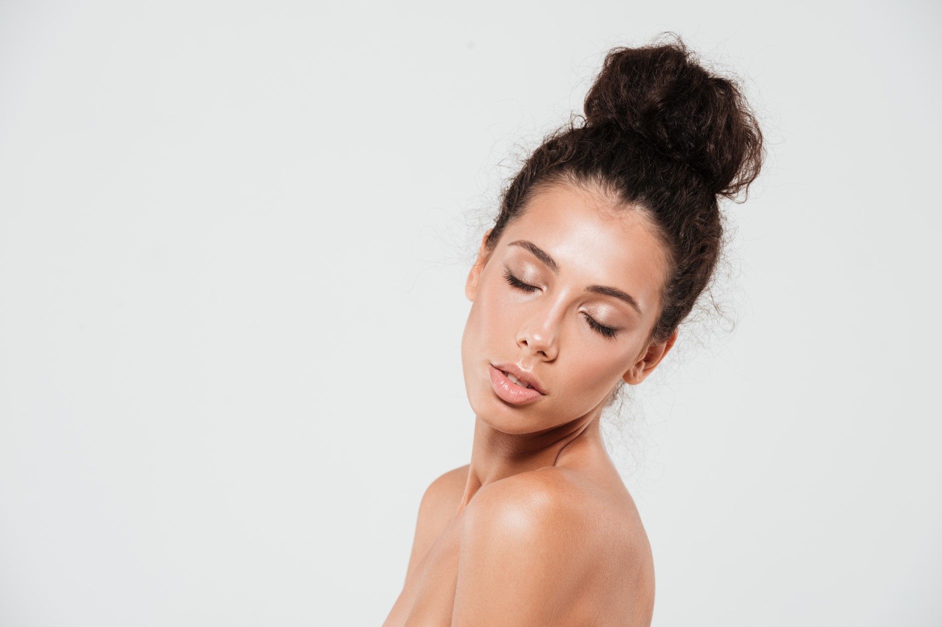 Woman with hair in a bun, eyes closed, against a plain light background.