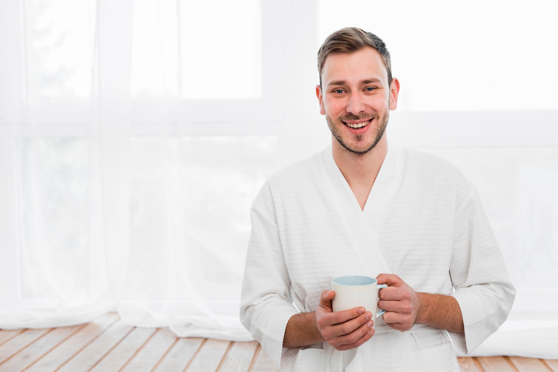a relaxed-looking man holding a cup and wearing white robes