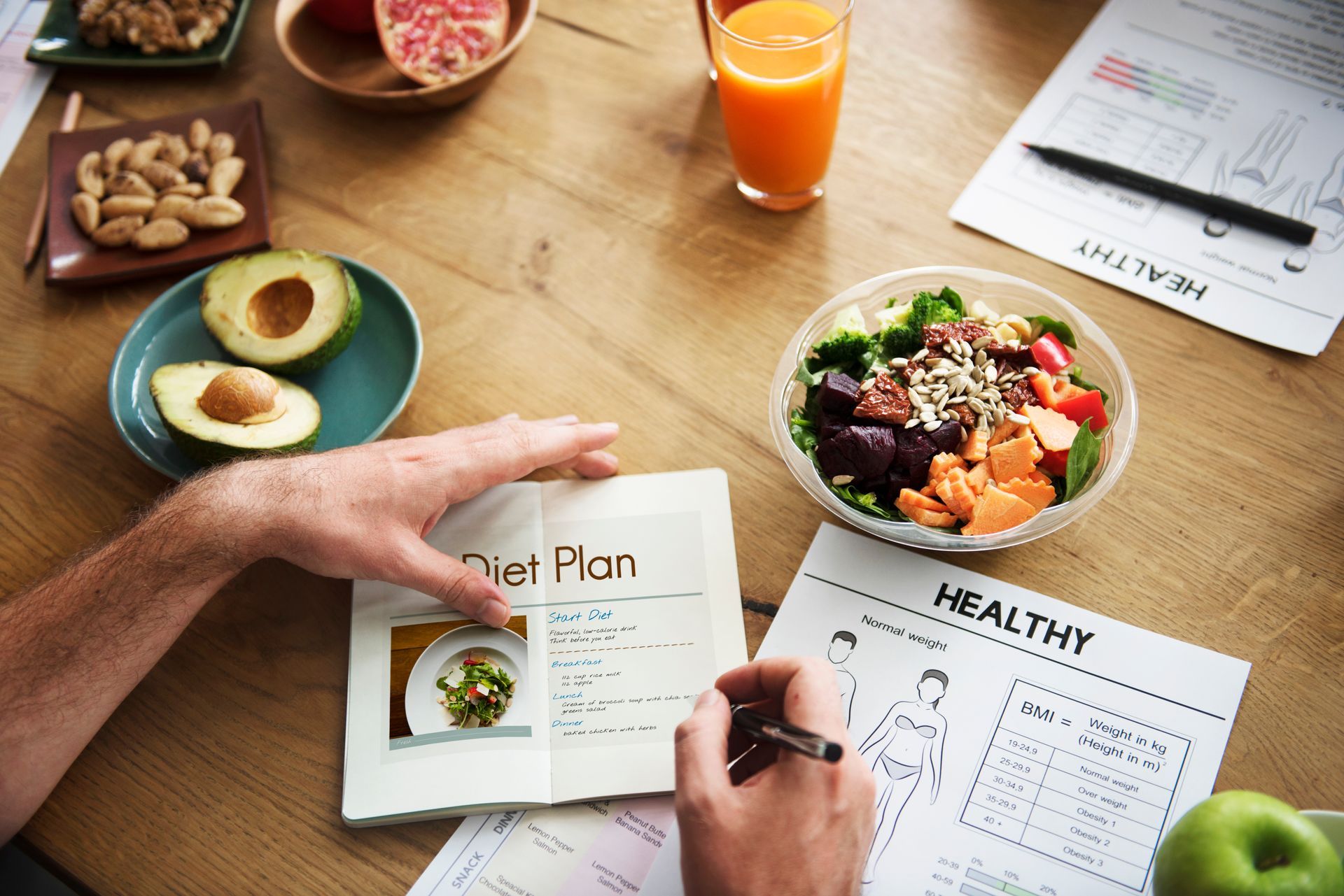 a man writing a diet plan with a health chart on the side. The table also has juice and a salad bowl, along with fruits