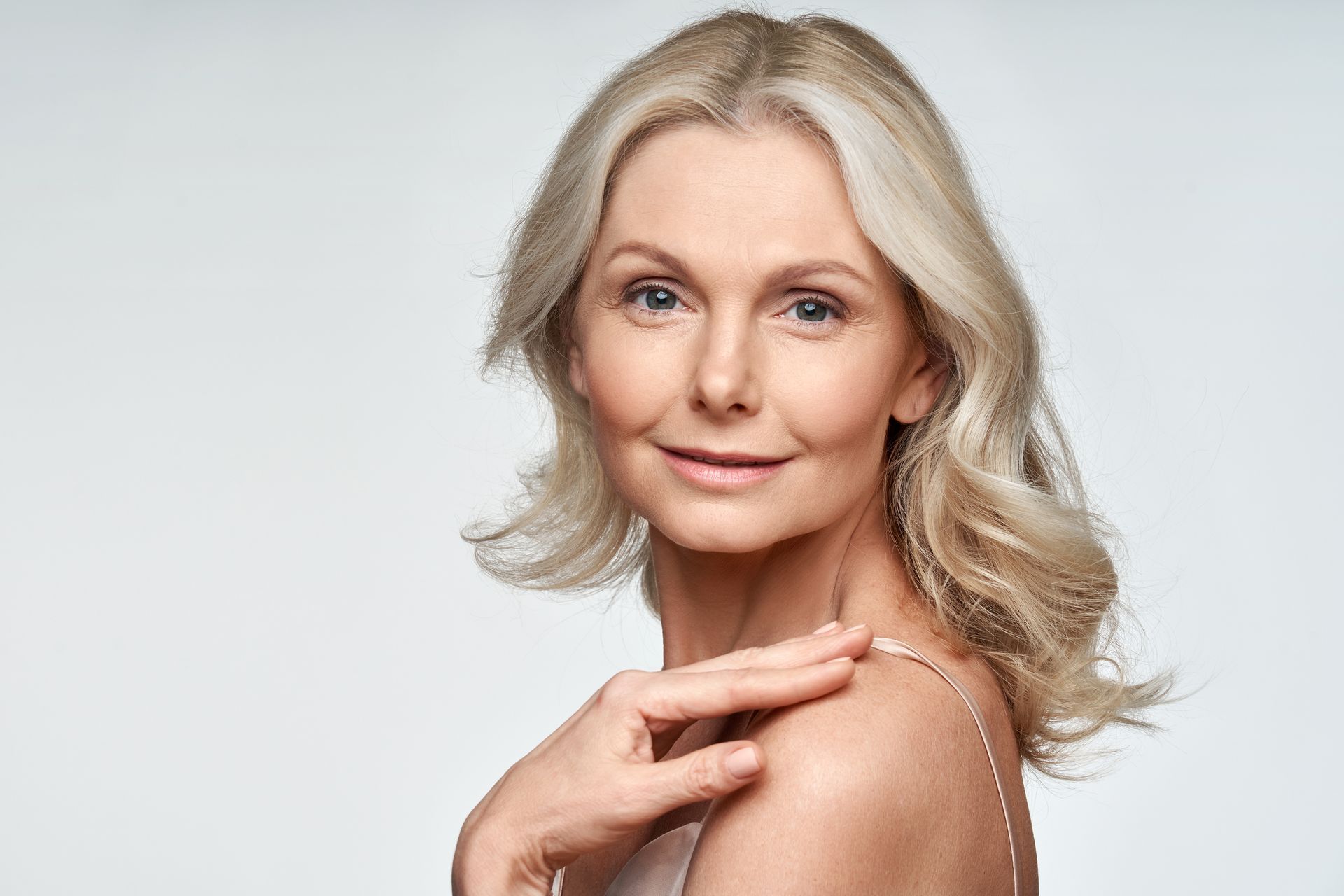 an old woman with radiant skin looking at the camera and touching her shoulder
