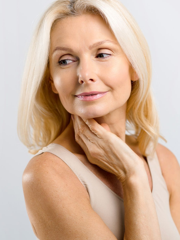 Blonde woman in a white top gently touching her neck against a light background