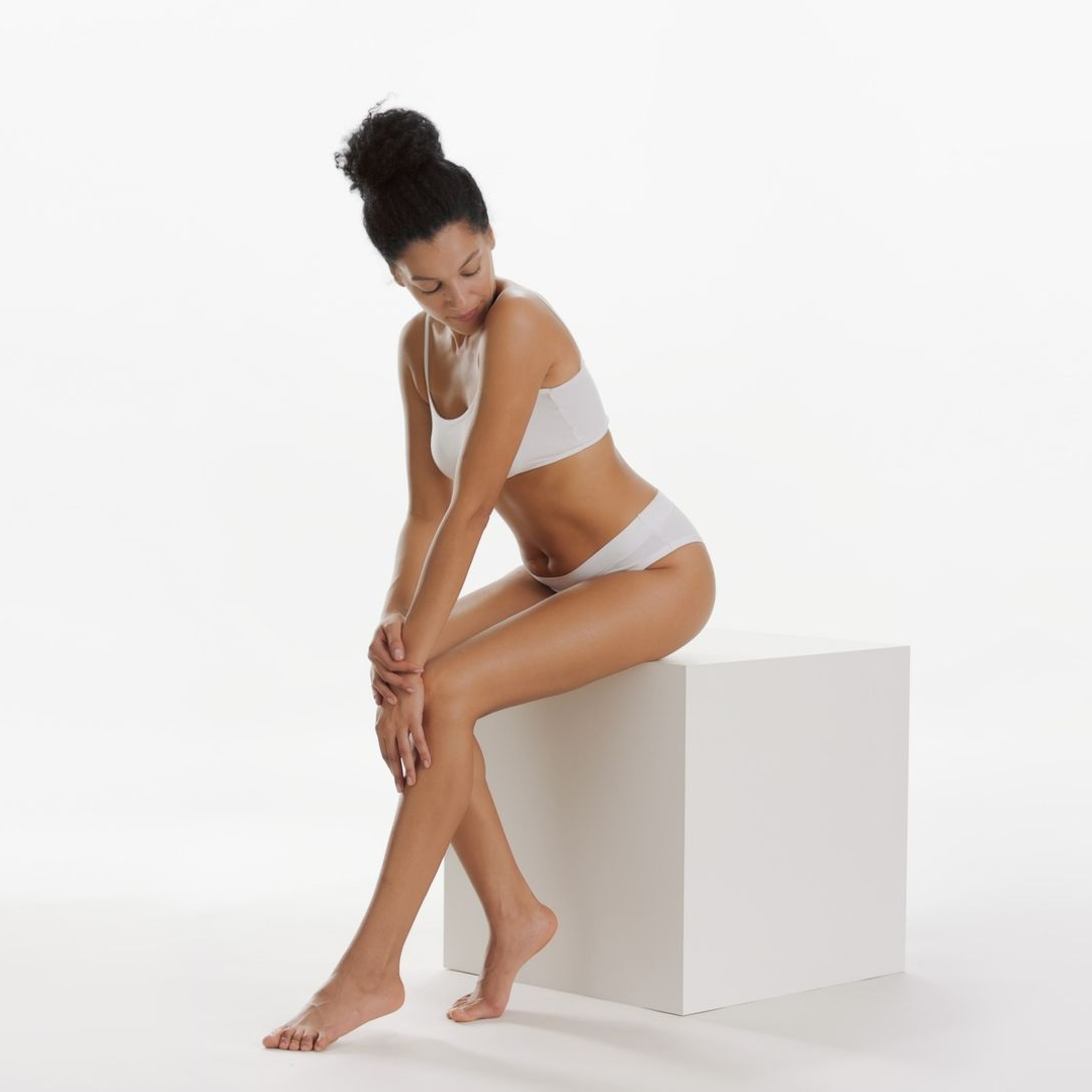 Woman in white lingerie sitting on a white block against a plain white background