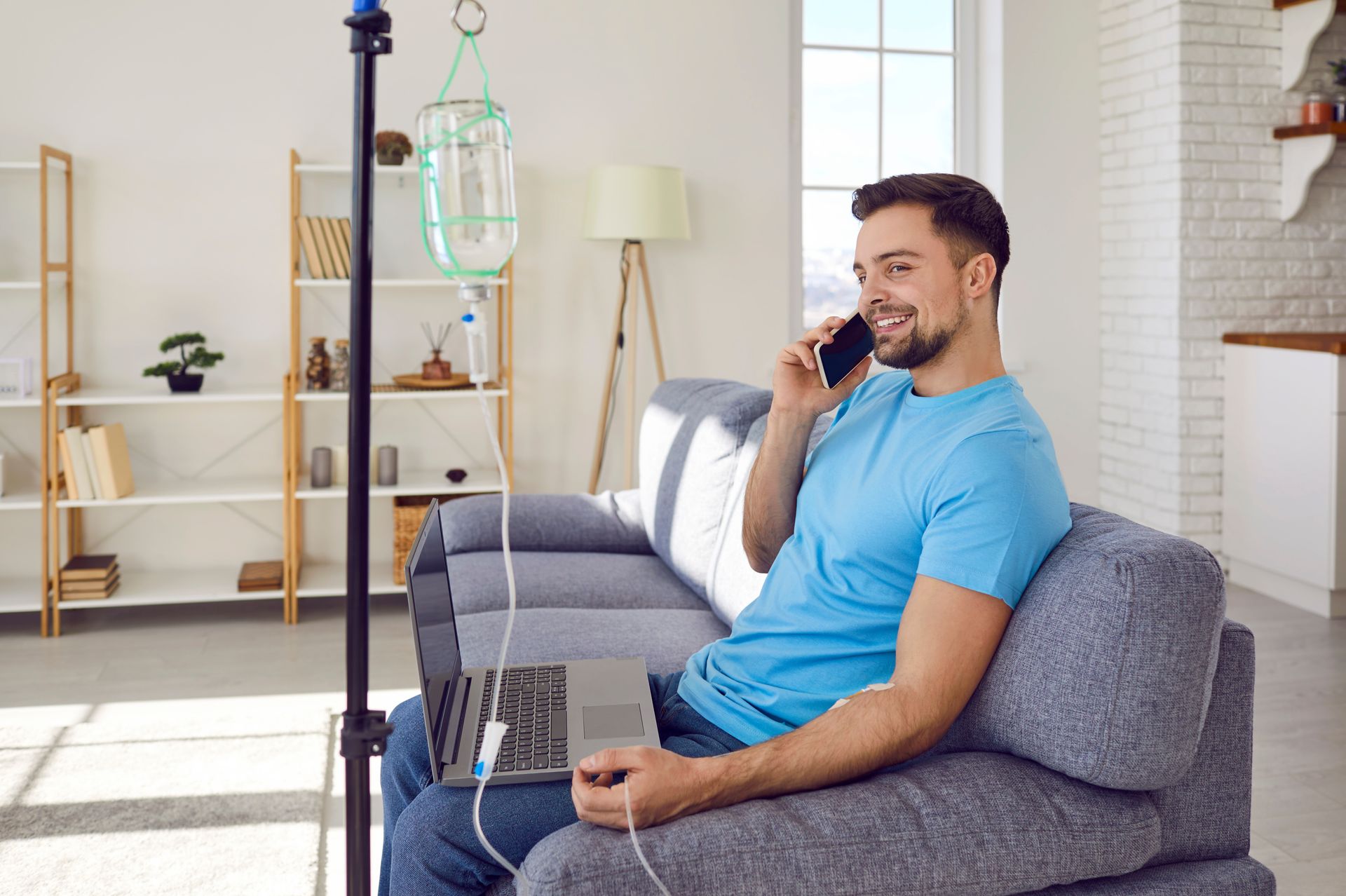a man sitting with his laptop and talking on the phone while getting an IV