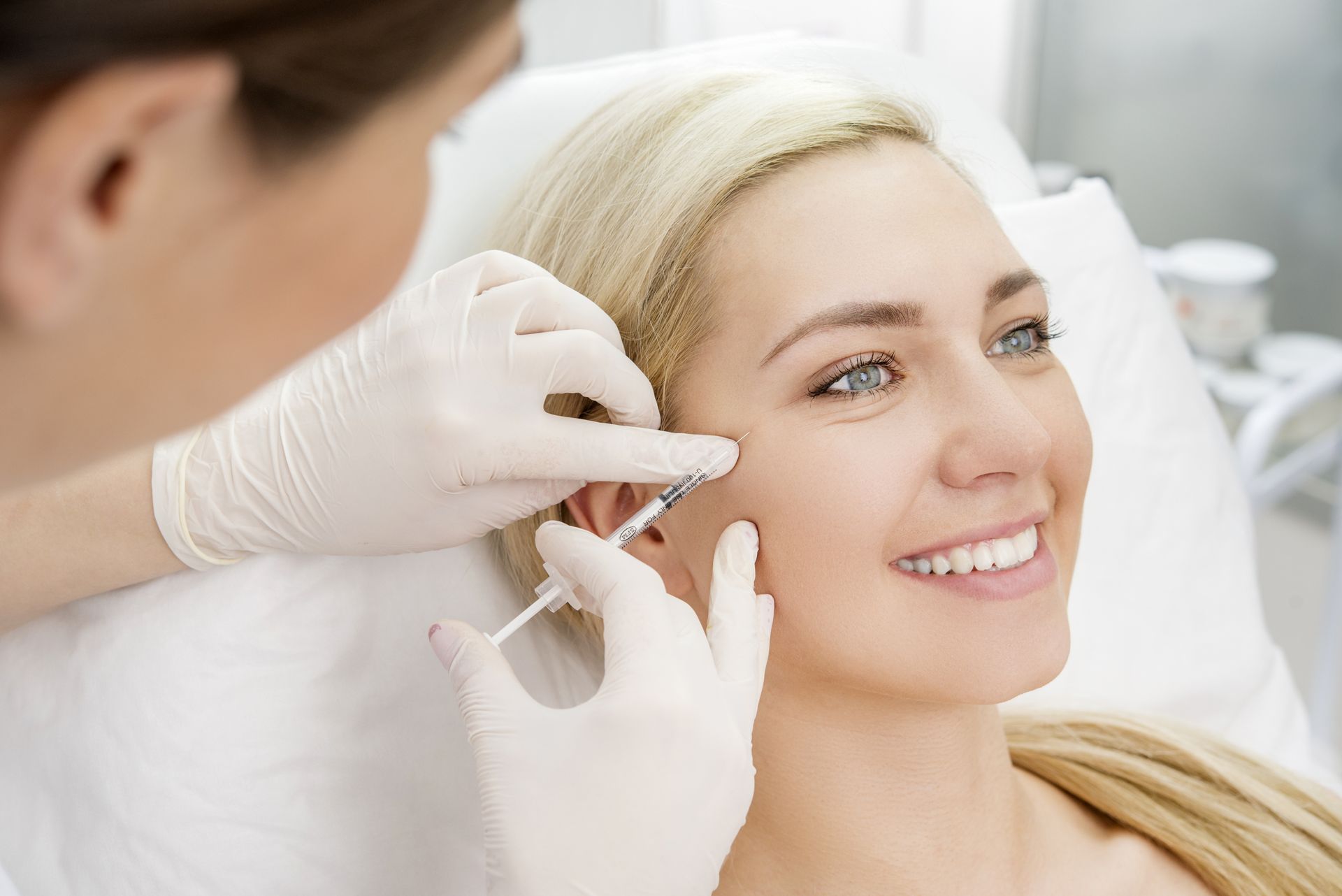 Medical professional applying facial treatment to a smiling woman lying on a treatment bed