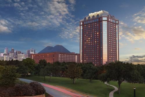 Tall brown hotel tower with smaller building, both against a skyline and park setting at sunset.