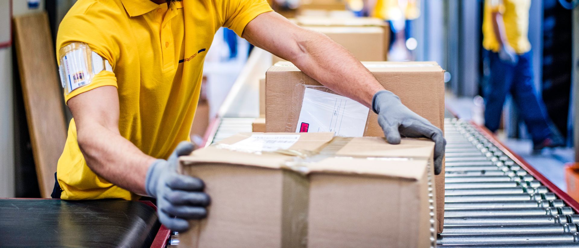 Un uomo con una maglietta gialla tiene in mano una scatola su un nastro trasportatore.