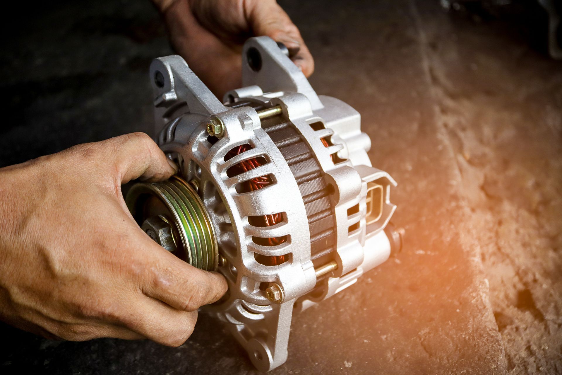 A mechanic is holding a car alternator in their hands.