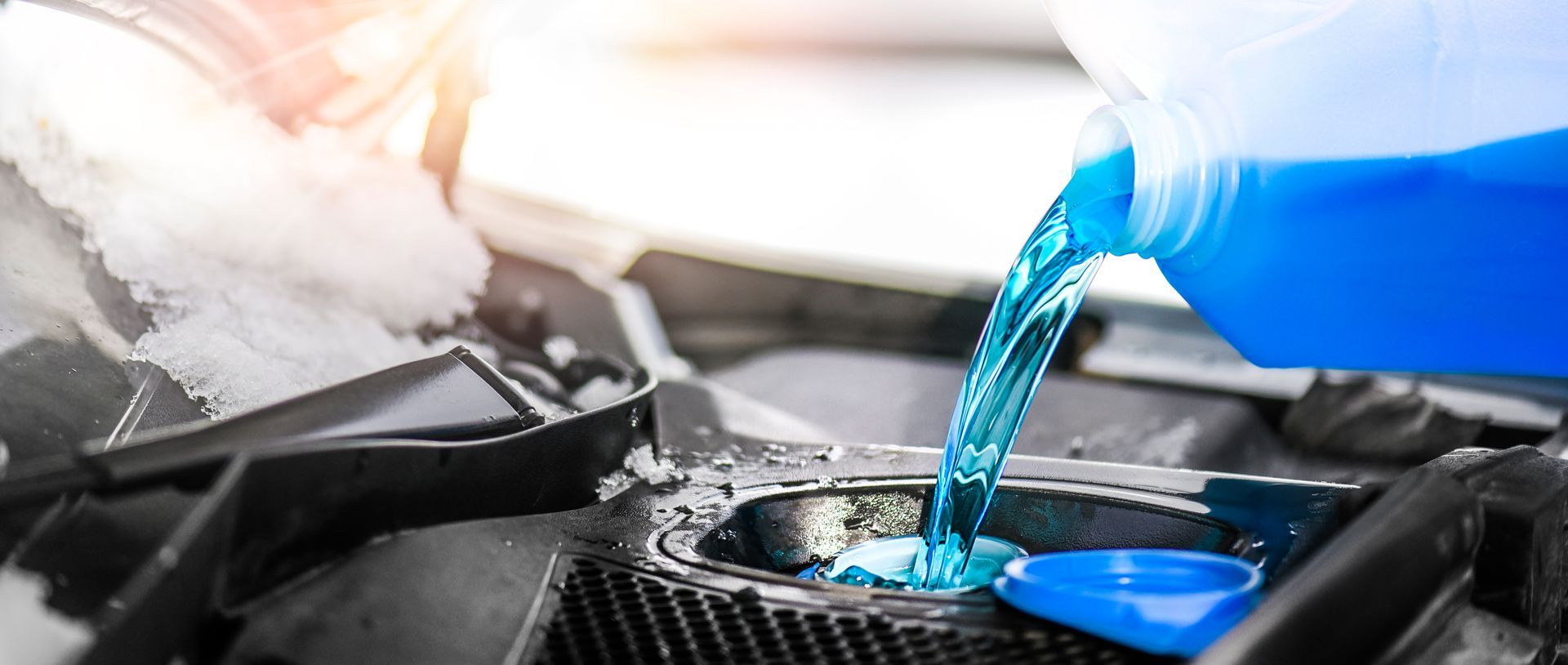 A mechanic is pouring a blue liquid into a car radiator