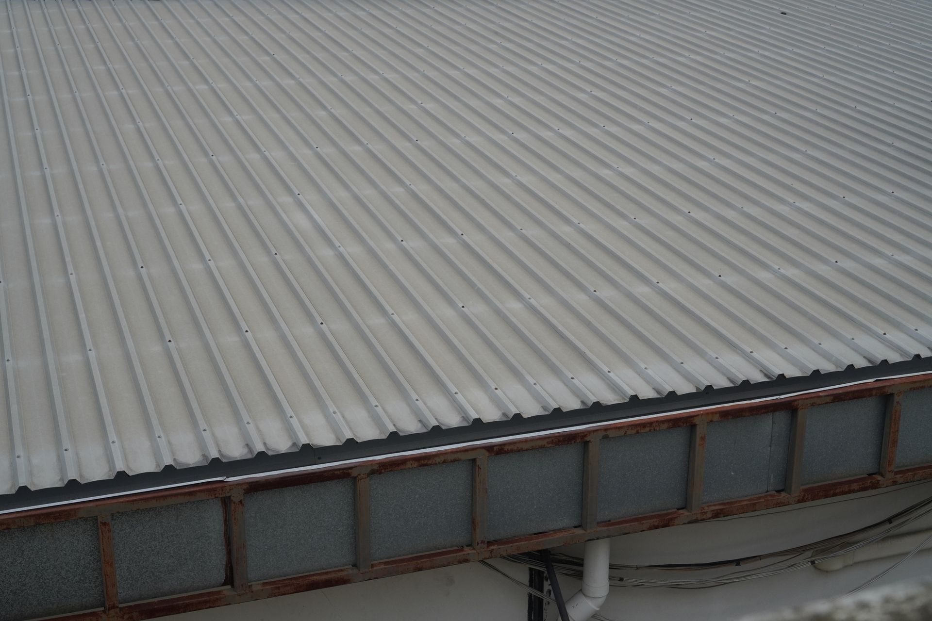 A white corrugated metal roof with a black gutter on a building.