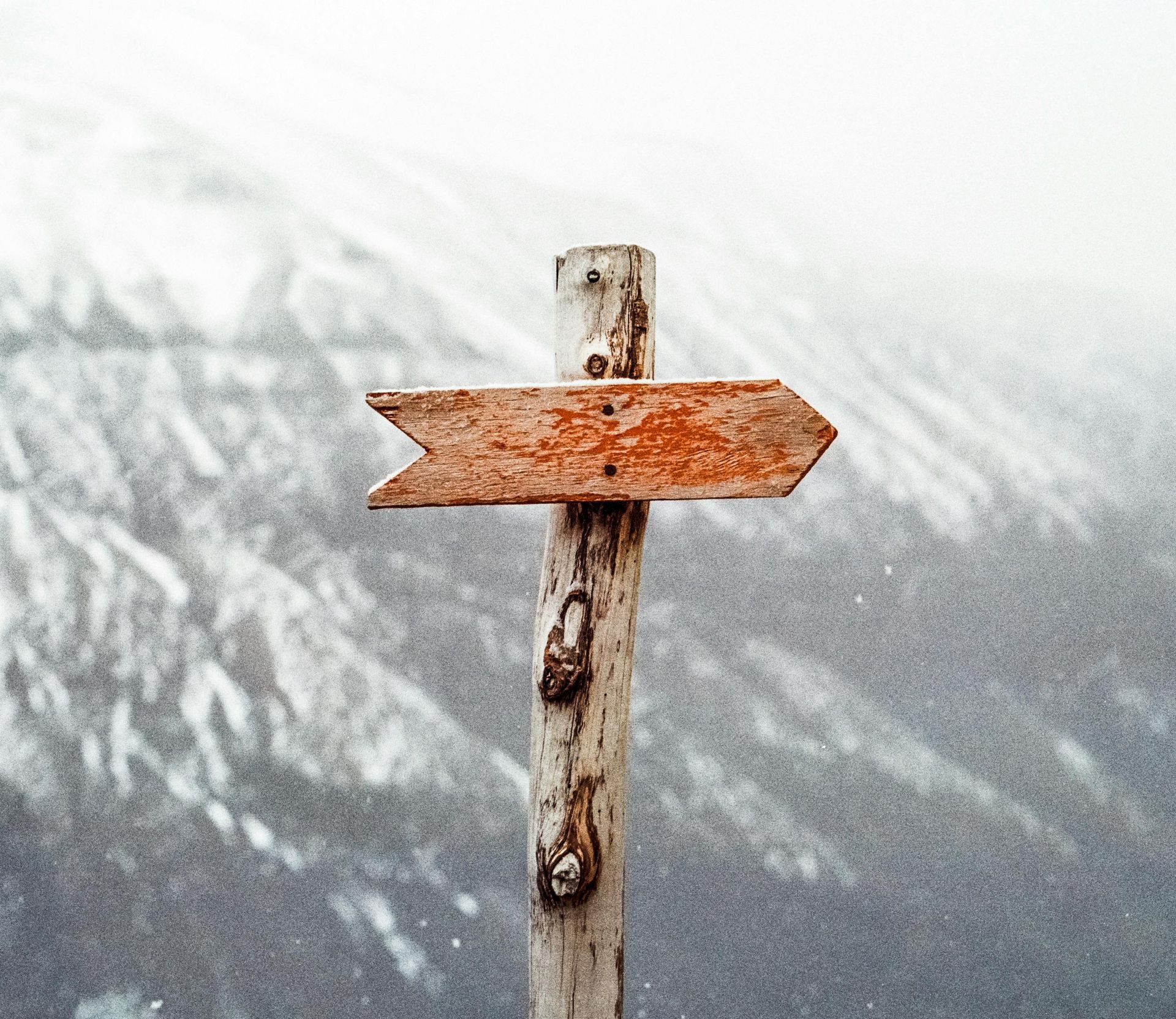 A wooden sign with an arrow pointing to the right in front of a snowy mountain.