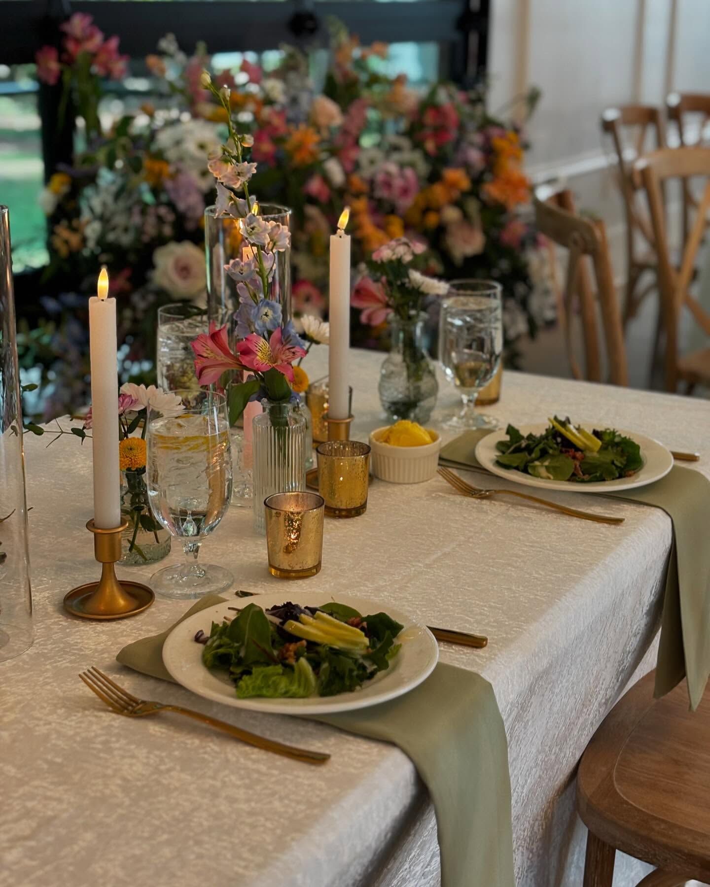 Elegant banquet table with white linens, floral centerpiece, candles, and plated salads with wine glasses