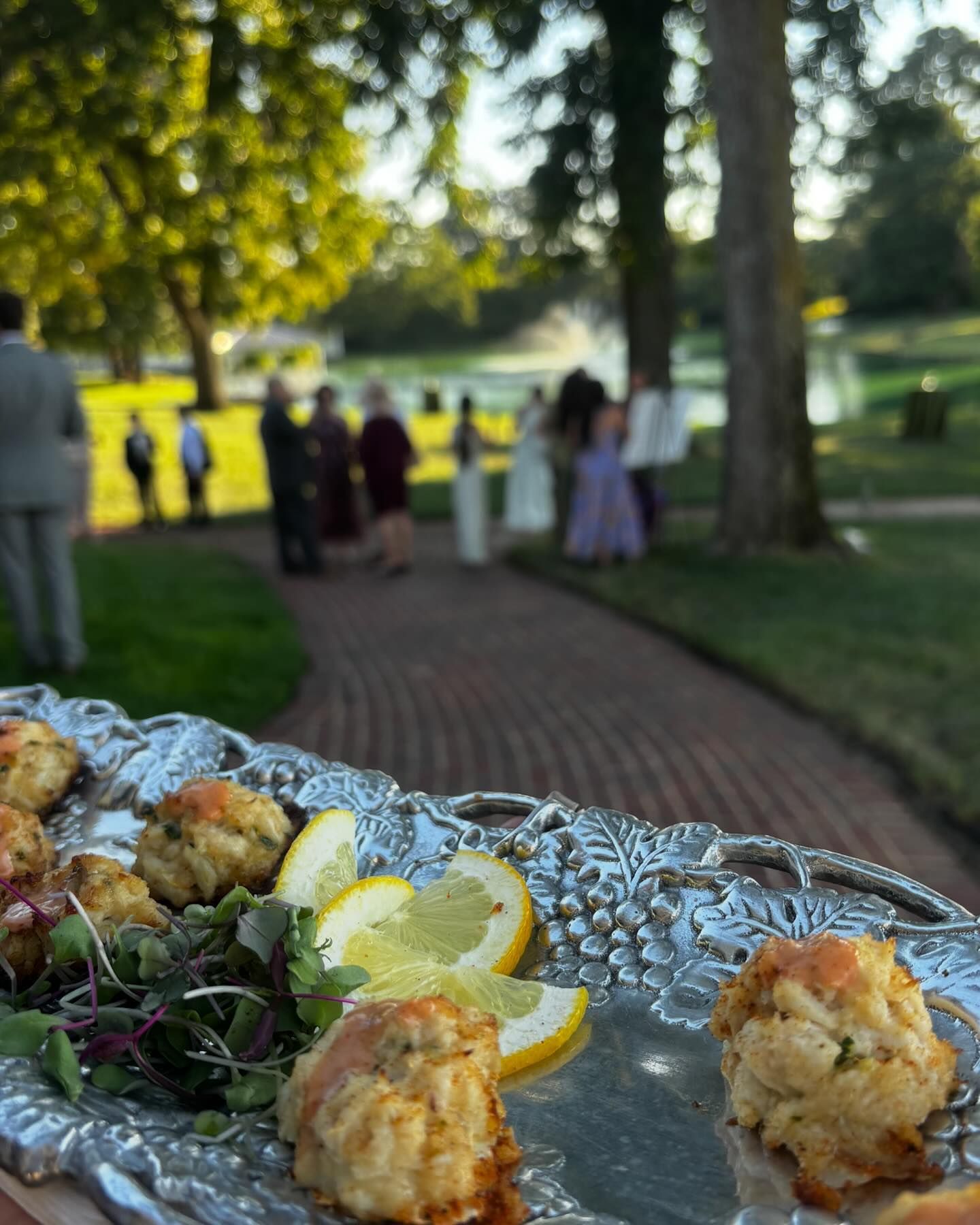 Appetizer platter with lemon slices in foreground, with people gathered at an outdoor evening event in the background