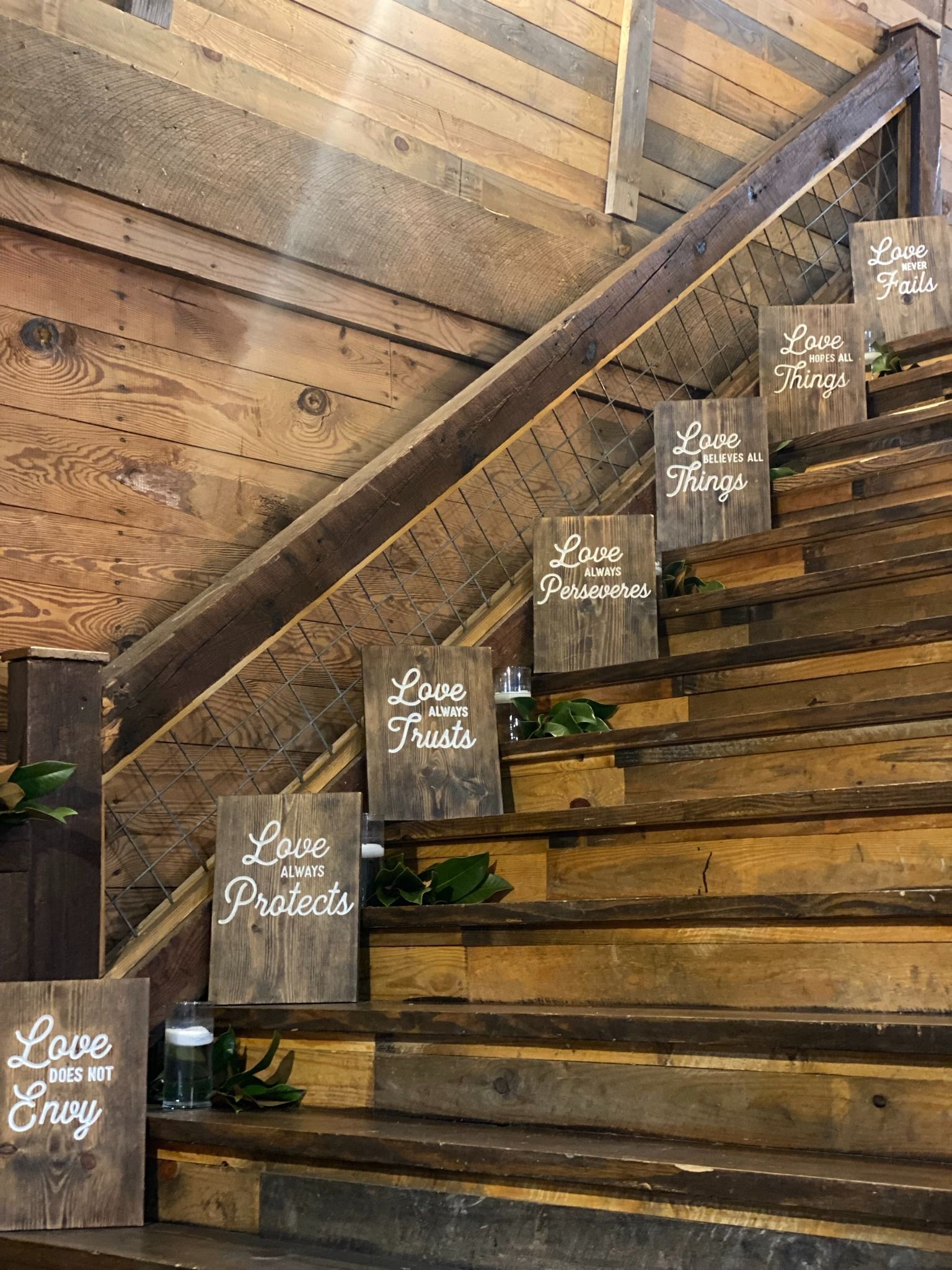 Wooden staircase decorated with small chalkboard signs and greenery along a rustic wall
