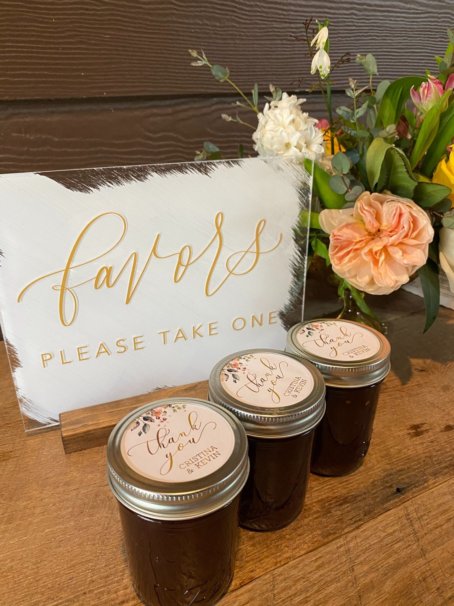 Favor jars with floral sign and white and peach flowers on a table