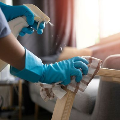 A person wearing blue gloves is cleaning a wooden table with a spray bottle.