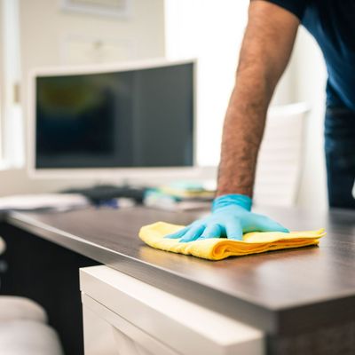 A man wearing blue gloves is cleaning a desk with a yellow cloth.