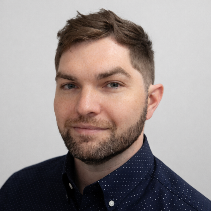 Man with short brown hair and beard, wearing a dark blue button-down shirt, looking at the camera.