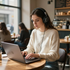 Vrouw typt op een laptop aan een cafétafel terwijl ze een koptelefoon draagt.