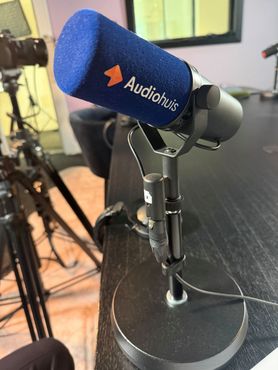 Zwarte koptelefoon rond een zilverkleurige studiomicrofoon op een houten tafel.