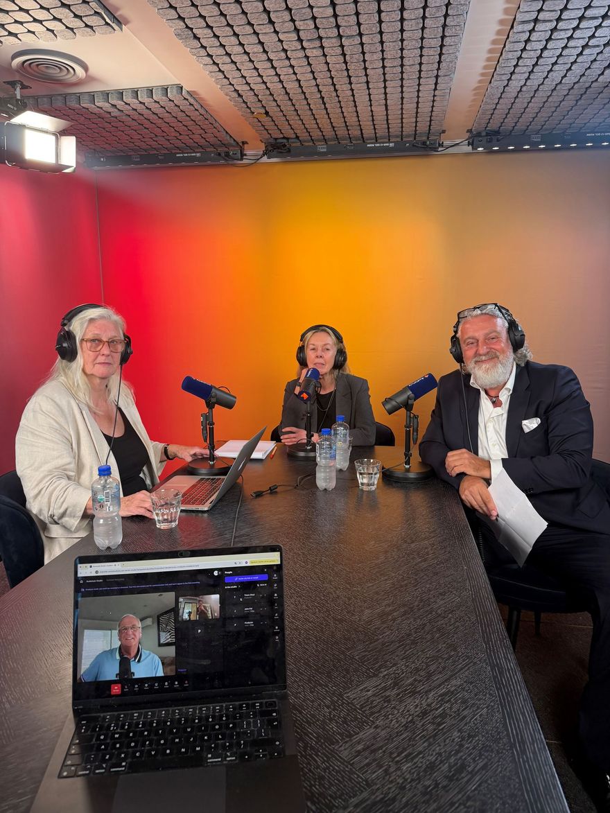 Drie mensen maken een podcast in een blauwe opnamestudio met microfoons en een laptop op tafel.