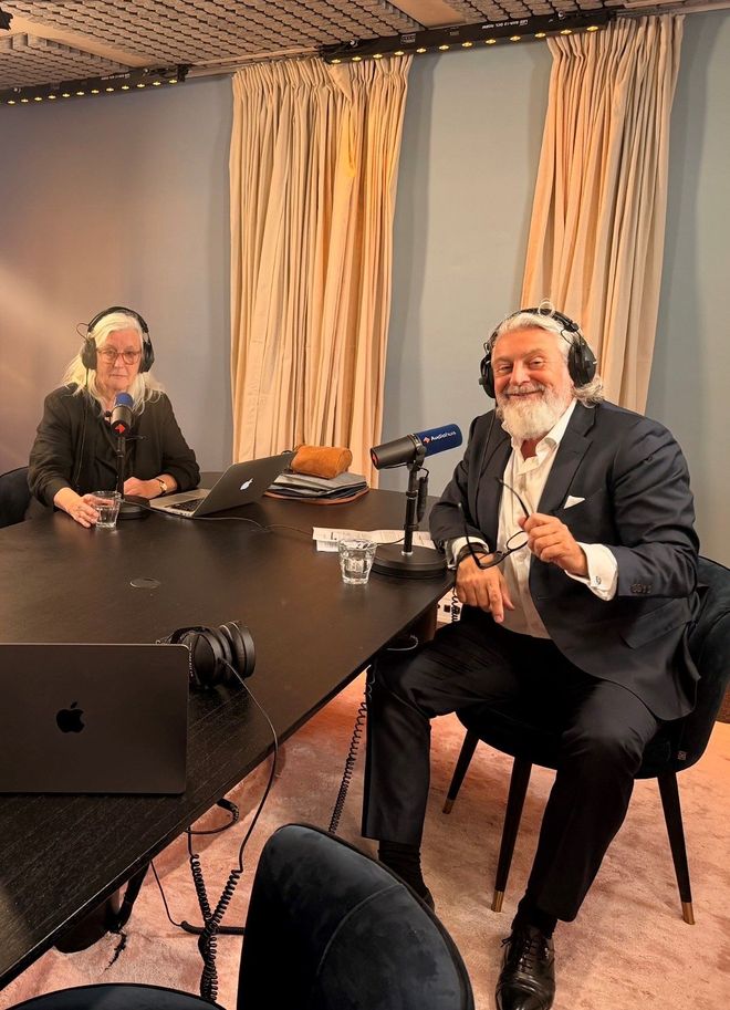 Drie mensen maken een podcast in een blauwe opnamestudio met microfoons en een laptop op tafel.