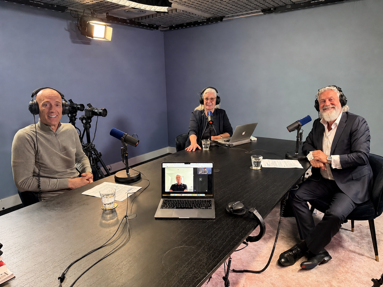 Drie mensen maken een podcast in een blauwe opnamestudio met microfoons en een laptop op tafel.