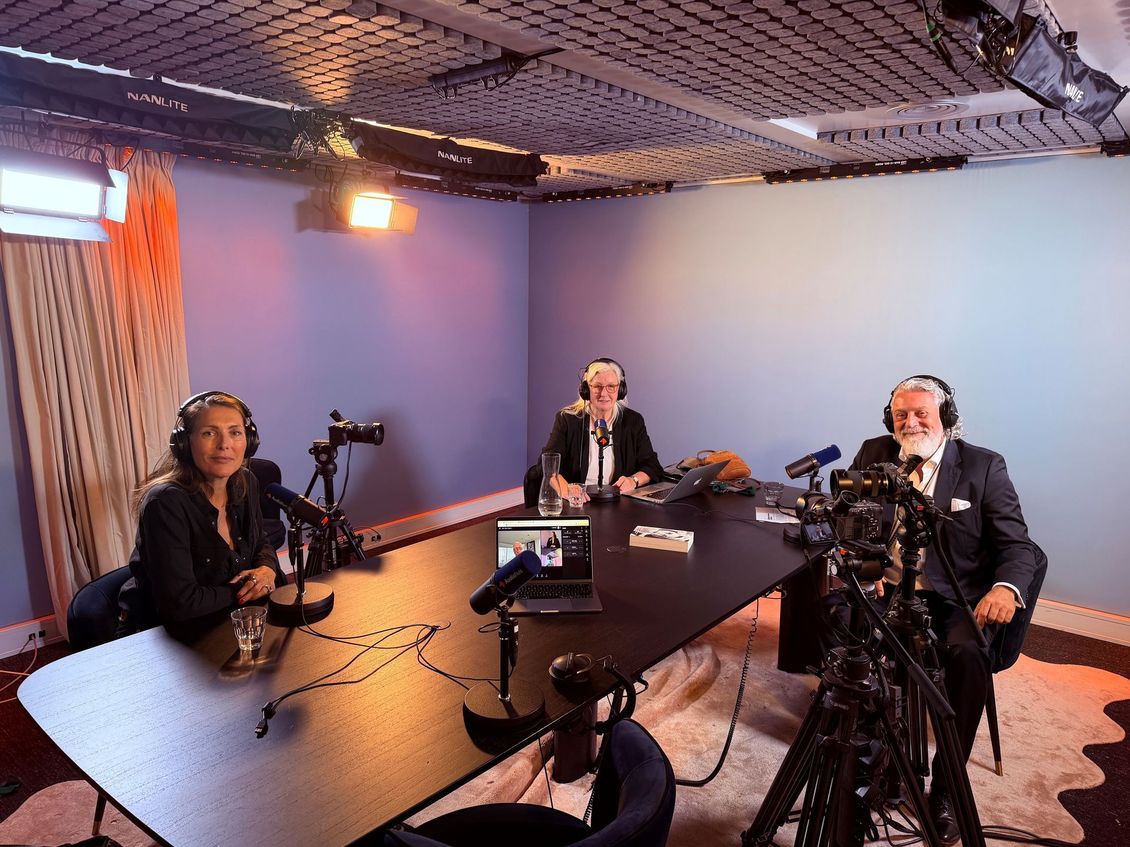 Drie mensen maken een podcast in een blauwe opnamestudio met microfoons en een laptop op tafel.