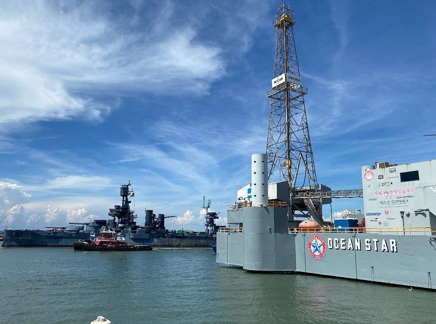 A large ship with a drilling rig on top of it is docked in the water.