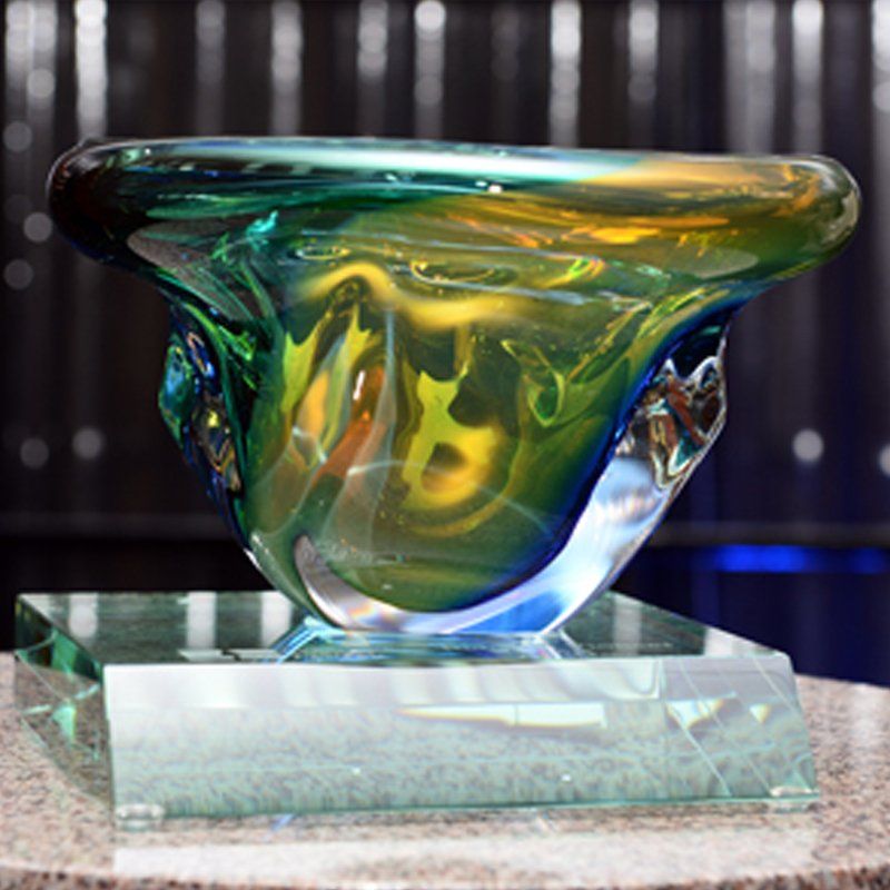 a green and yellow glass bowl is sitting on a glass base