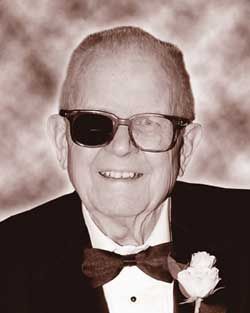 A man wearing sunglasses and a bow tie is smiling in a black and white photo.